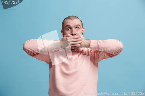 Image of The young man whispering a secret behind her hand over blue background