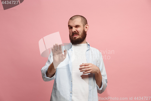 Image of Young man with disgusted expression repulsing something, isolated on the pink