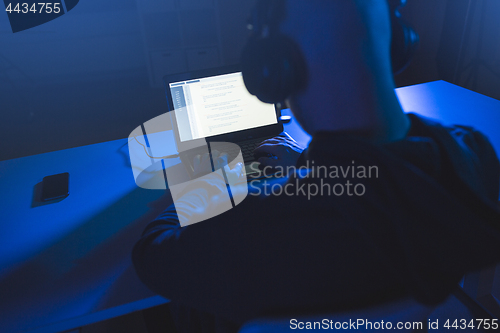 Image of hacker with coding on laptop computer in dark room