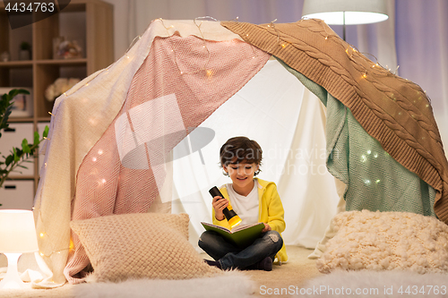 Image of happy little boy reading book in kids tent at home