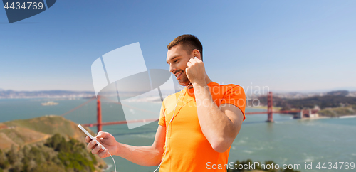 Image of man with smartphone and earphones over golden gate