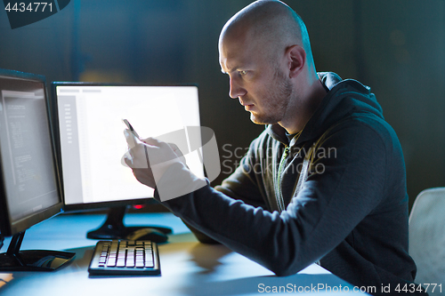 Image of hacker with smartphone and computers in dark room