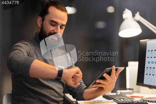 Image of man with smartwatch and tablet pc at night office