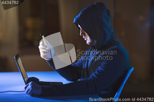 Image of hacker with laptop and smartphone in dark room