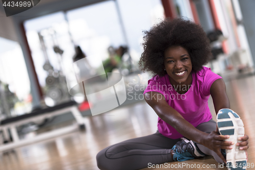 Image of woman in a gym stretching and warming up man in background worki