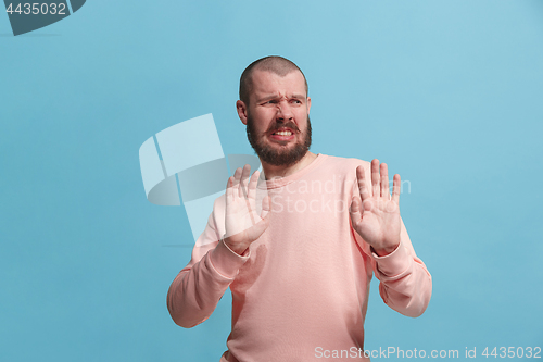 Image of Young man with disgusted expression repulsing something, isolated on the pink