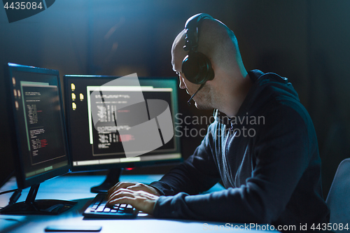 Image of hacker with coding on laptop computer in dark room