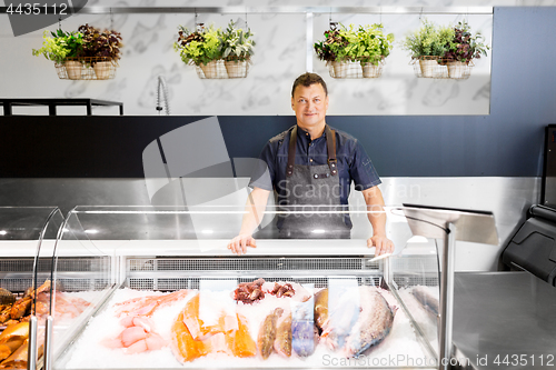 Image of male seller with seafood at fish shop fridge