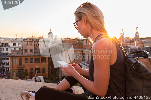 Image of Female tourist taking mobile phone photo of Piazza di Spagna, landmark square with Spanish steps in Rome, Italy at sunset.
