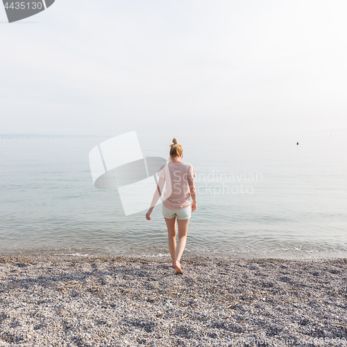 Image of Happy Carefree Woman Enjoying Sunset Walk on White Pabbled Beach.