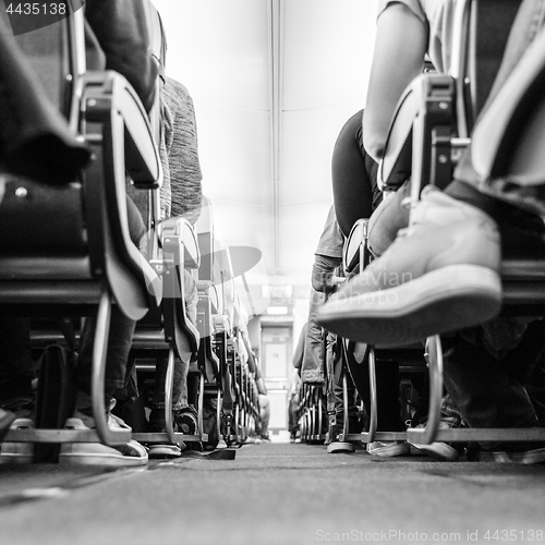 Image of Low agle view of passenegers commercial airplane aisle with passenegers sitting on their seats while flying. Black and white photo.