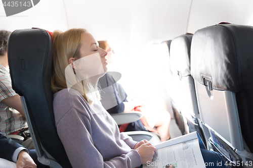 Image of Tired blonde casual caucasian lady napping on seat while traveling by airplane. Commercial transportation by planes.