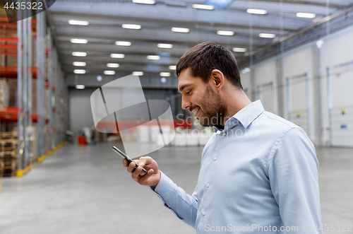 Image of businessman with smartphone at warehouse