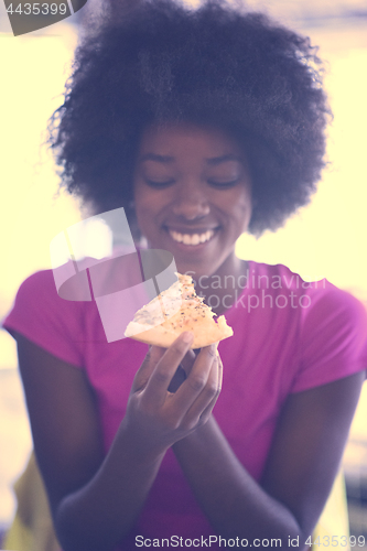Image of woman with afro hairstyle eating tasty pizza slice