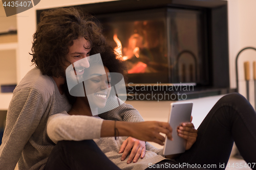 Image of multiethnic couple using tablet computer on the floor