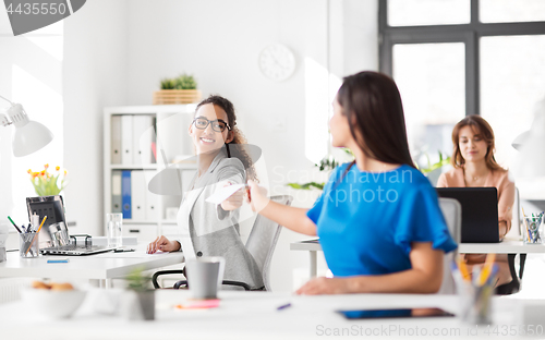 Image of businesswomen giving each other papers at office