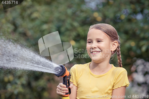 Image of Happy little girl pouring water from a hose.