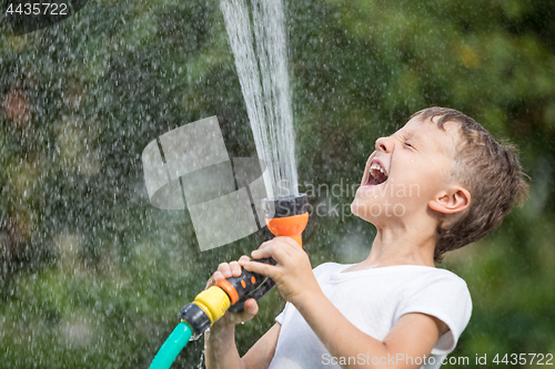 Image of Happy little boy pouring water from a hose.