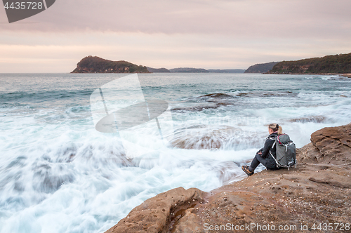 Image of Woman sitting by the ocean letting waves lap at her feet