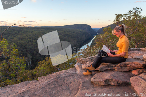 Image of A woman sitting on a rock reading in nature