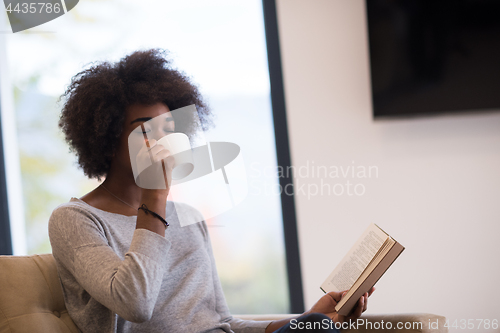 Image of black woman reading book  in front of fireplace