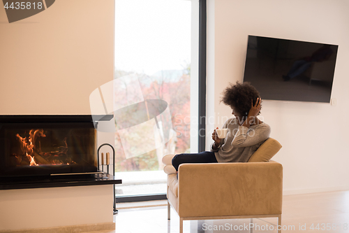 Image of black woman drinking coffee in front of fireplace