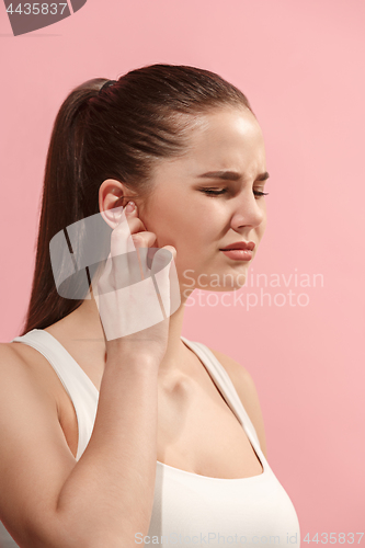 Image of The Ear ache. The sad woman with headache or pain on a pink studio background.