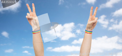 Image of hands with gay pride rainbow wristbands make peace