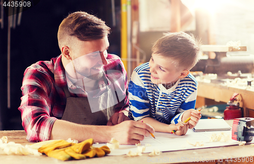 Image of happy father and son with blueprint at workshop