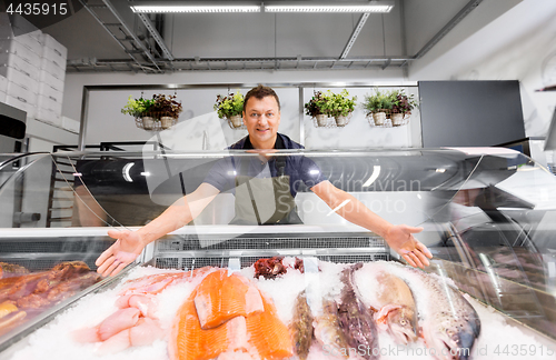 Image of male seller showing seafood at fish shop fridge