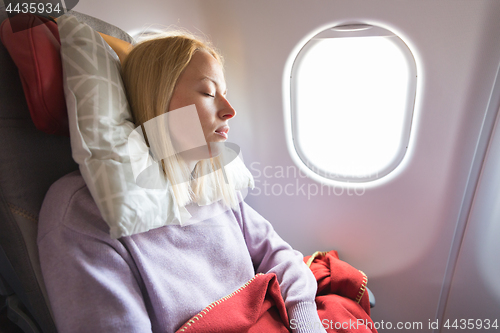 Image of Tired blonde casual caucasian lady napping on seat while traveling by airplane. Commercial transportation by planes.