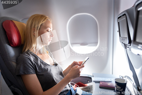 Image of Woman listening to music on smart phone on commercial passengers airplane during flight.