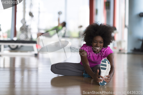 Image of woman in a gym stretching and warming up man in background worki