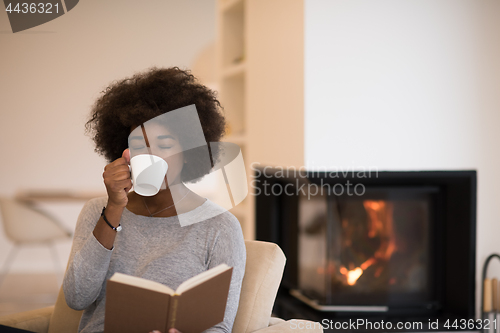 Image of black woman reading book  in front of fireplace