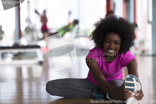 Image of woman in a gym stretching and warming up man in background worki