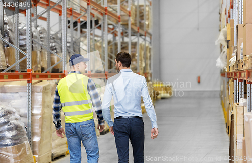 Image of worker and businessman walking along warehouse