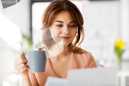 Image of businesswoman with papers drinks coffee at office