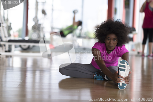 Image of woman in a gym stretching and warming up man in background worki