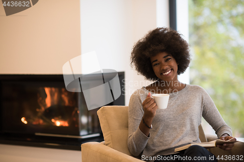 Image of black woman reading book  in front of fireplace