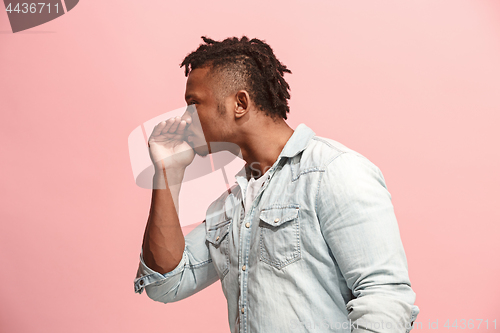 Image of The young man whispering a secret behind her hand over pink background