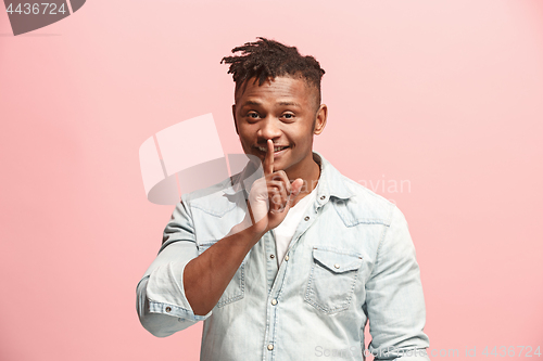 Image of The young man whispering a secret behind her hand over pink background