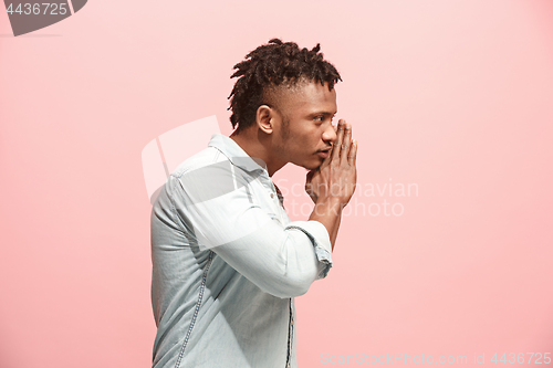 Image of The young man whispering a secret behind her hand over pink background