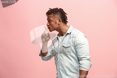 Image of The young man whispering a secret behind her hand over pink background