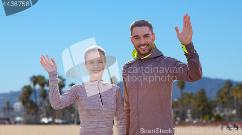 Image of smiling couple in sport clothes waving hand