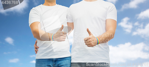 Image of gay couple with rainbow wristbands shows thumbs up