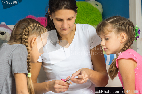 Image of Mom shows daughters how to cut out a hand-made paper from a colored paper