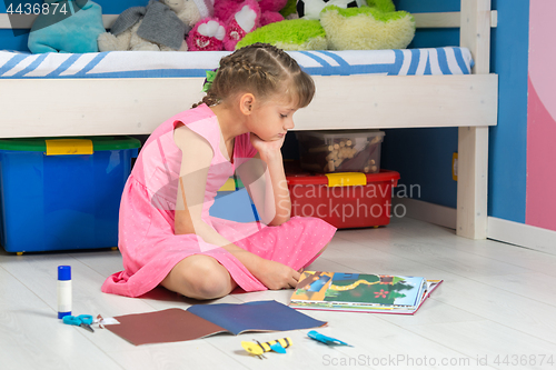 Image of A girl chooses a hand-made article in her book to make it from a colored paper