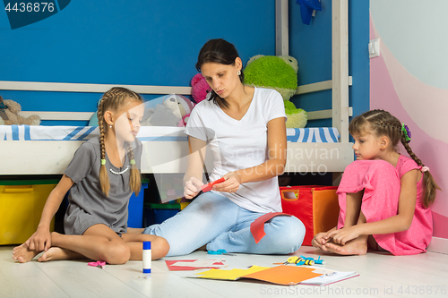 Image of Mom explains to daughters how correctly to cut out figures from colored paper