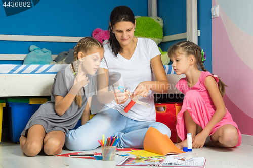 Image of Mom shows daughters how to cut out figures from colored paper