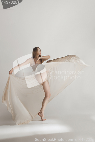 Image of Young beautiful dancer in beige swimsuit dancing on gray background